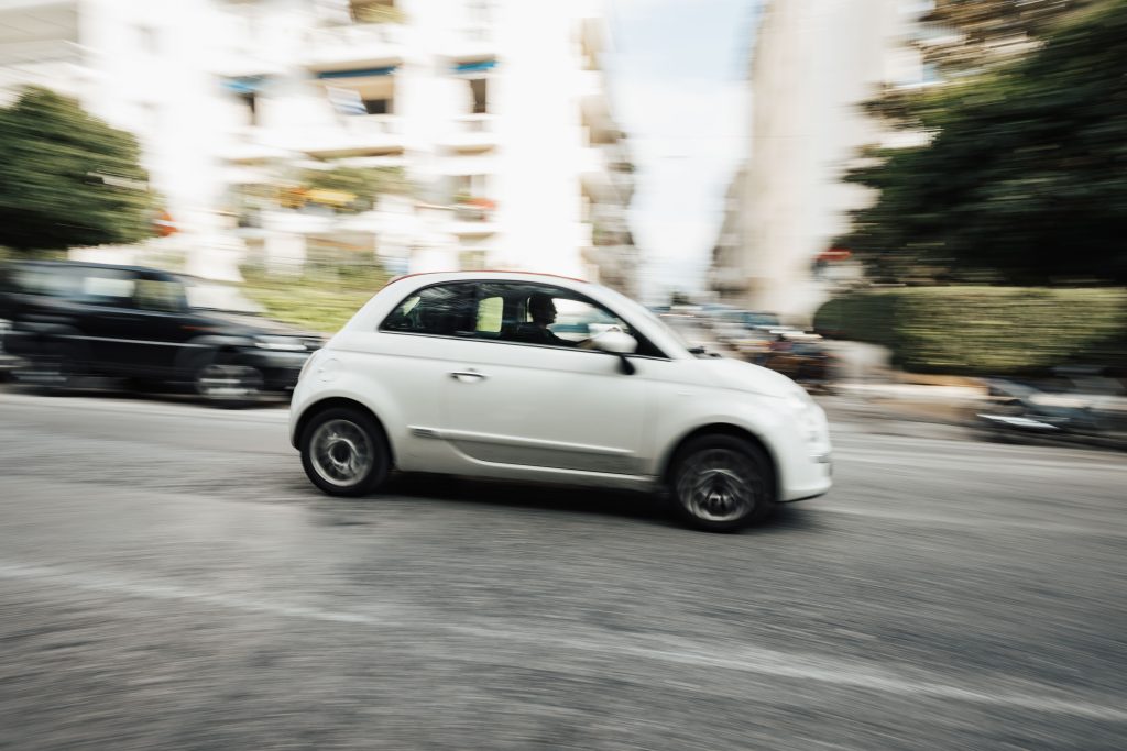Dynamic capture of a compact white car speeding through a city street with motion blur effect.