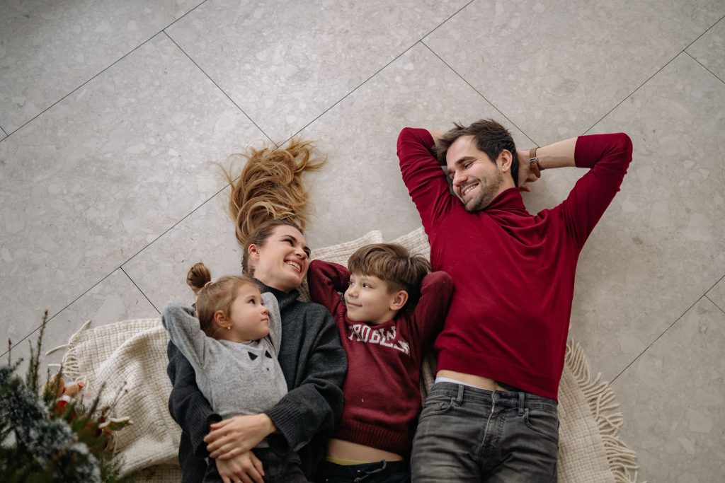 Smiling family of four lying on a blanket, sharing happiness and love indoors.