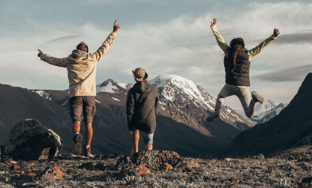 Three people enjoying a hike in snow-capped mountains, jumping with joy filled with adventure.